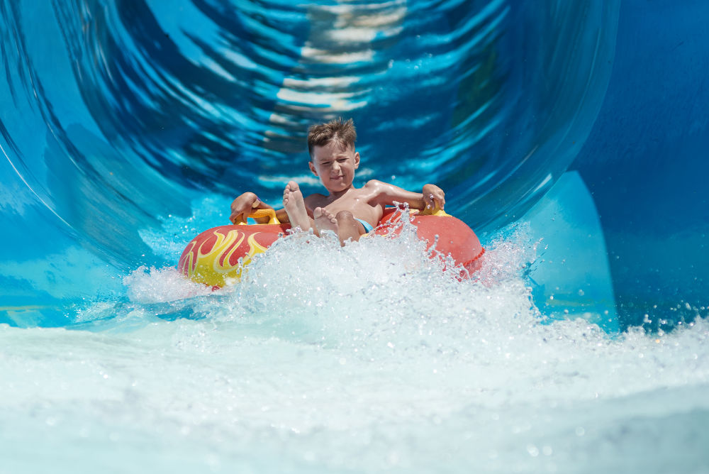 Young boy coming down a water slide on a red and yellow tube