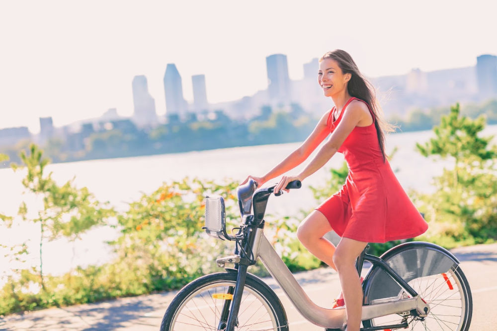 Woman in rad dress on a bike with water and San Antonio behind her